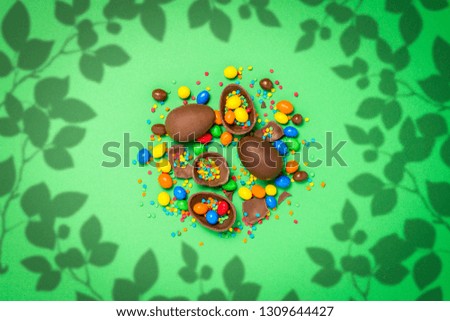 Broken and whole chocolate Easter eggs, multicolored sweets ,green background. Shrub. Concept of celebrating Easter, Easter decorations. Flat lay, top view. Copy Space. Happy Easter.