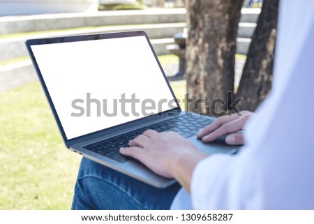 Mockup image of a woman using and typing on laptop with blank white screen , sitting in the outdoors with nature background
