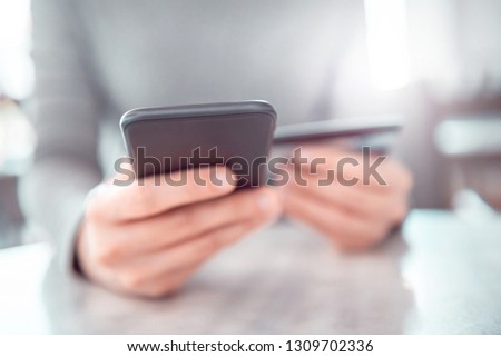 Young woman shopping online with credit card using smartphone at home. Indoor.