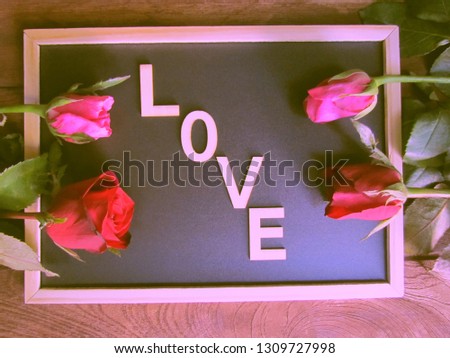Red and pink roses placed on the blackboard and with letters made of wood, placed as love words on the blackboard on the wooden background. Concept love and couples. Vintage tone