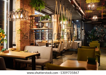Interior of contemporary cozy cafe with several wooden tables, chairs and sofas prepared for guests Royalty-Free Stock Photo #1309735867