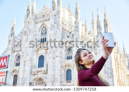 Smiling girl takes a selfie with her mobile in fron of the Duomo of Milan during the day