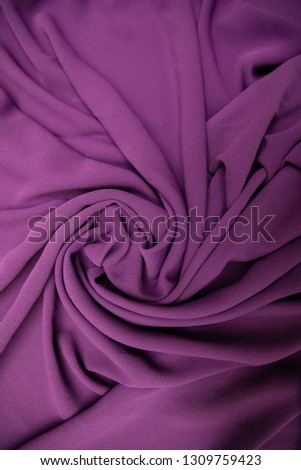Purple fabric spread out on the table and slightly twisted.