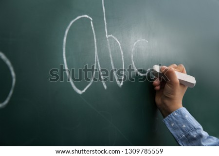 Little child writing letters on chalkboard, closeup