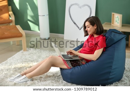 Young woman with laptop sitting on beanbag chair at home