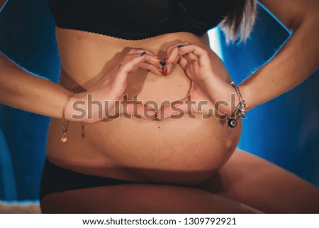 Pregnant woman holding belly , hugging tummy, making symbol heart hands at home. Baby Shower. Motherhood concept. 