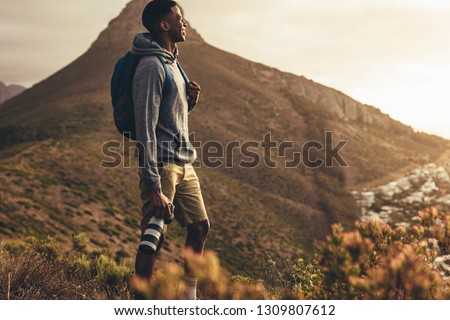 Young man standing on mountain trail with his dslr camera and looking at the view. Social media influencer on hiking trip for new content for his channel.