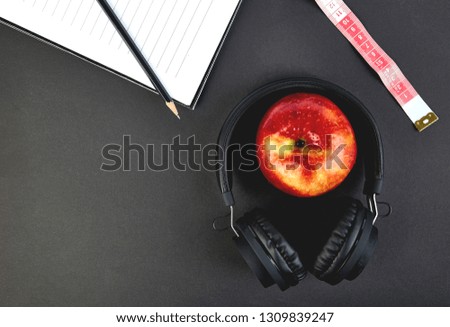 Black Headphones and red  apple with notebook, note, measuring tape on black background. Flat lay. Top view. Copy space. Diet concept.