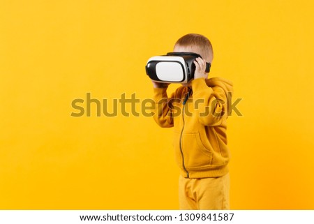 Little fun kid boy 3-4 years old wearing yellow clothes and headset of vr on eyes isolated on orange wall background, children studio portrait. People, childhood lifestyle concept. Mock up copy space