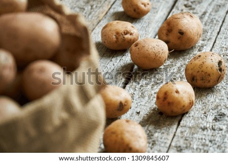 Raw unpeeled potatoes tubers on the rough wooden boards of a country table with a blurred burlap sack on the foreground
