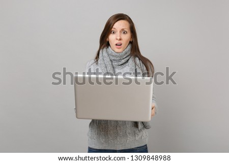 Perplexed young woman in gray sweater, scarf working on laptop pc computer isolated on grey wall background. Healthy lifestyle, online treatment consulting, cold season concept. Mock up copy space