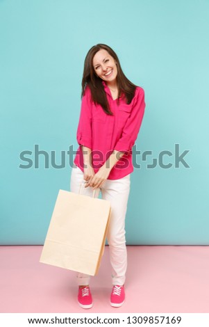 Full length portrait smiling young woman in rose shirt blouse, white pants hold shopping bags isolated on bright pink blue pastel wall background studio. Fashion lifestyle concept. Mock up copy space