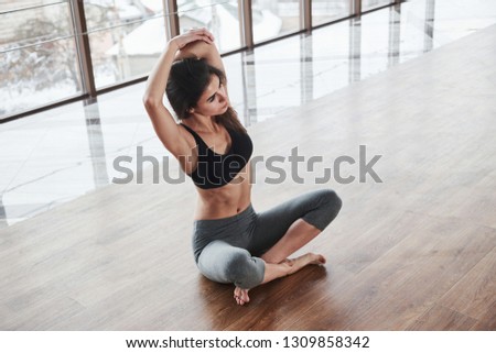 Hands above the head. Relaxed cute young girl sits on the floor in gym with big windows.