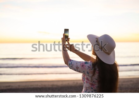 Traveler young woman is shooting video of beautiful sunset landscape on mobile phone camera. Summer vacation travel and holiday.