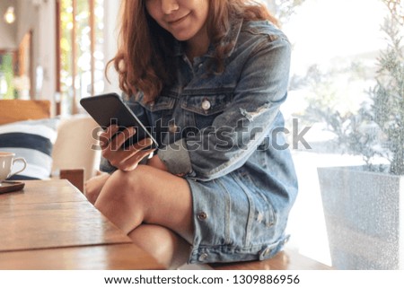 Closeup image of a beautiful asian woman holding , using and looking at smart phone in cafe