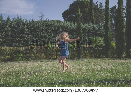 little girl with long blond hair dancing outdoors in meadow full of daisies