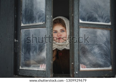A child in the village opens the windows in winter and looks out onto the street.