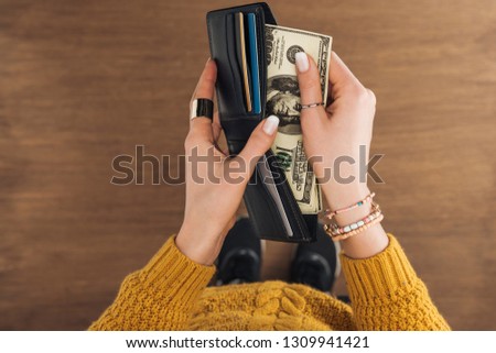 top view of woman taking from wallet dollars banknotes on wooden background
