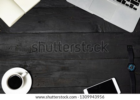 Work place flat lay on black background. Laptop, note pad, coffee and cell phone on lack wood texture, top view