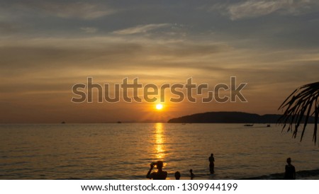 Beautiful scenery sunset with glowing orange light painted on cloudy sky become to twilight dawn, above the sea, long tail boat and black mountain, people enjoy evening time on beach in Thailand