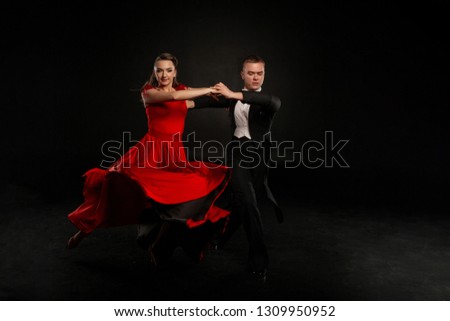 Beautiful couple in the active ballroom dance, girl in red dress and man in black suit. Studio photo on grey background