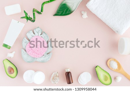 Layout of green white pink spa and wellness frame with towel, bamboo, tropical leaves , avocado, bottle of oil, body and face care tools on pastel background. Flat lay, top view.
