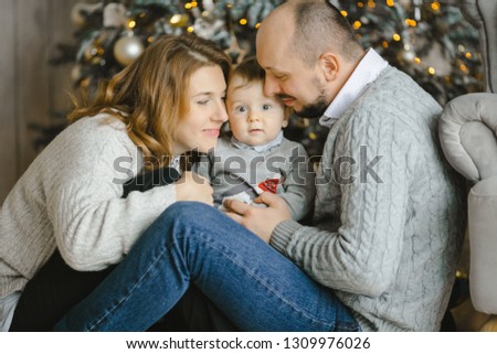 Christmas family portrait. Charming man, woman and their little son have fun posing before a Christmas tree in a bright room