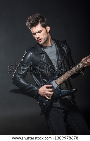 handsome rocker in leather jacket playing electric guitar isolated on black