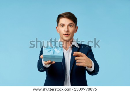 Cute man in a suit with a gift in his hands on a blue background
