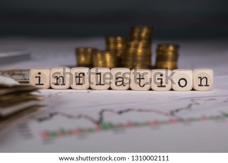 Word INFLATION composed of wooden letter. Stacks of coins in the background. Closeup