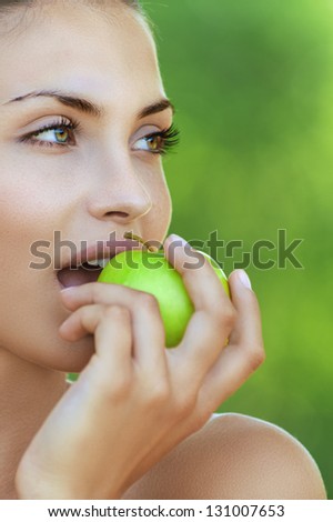 Portrait of beautiful young woman with apple, against background of summer green park.