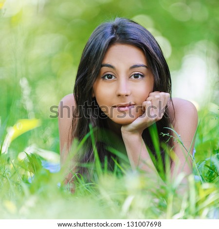 Beautiful dark-haired young woman lying on grass, against summer green park.