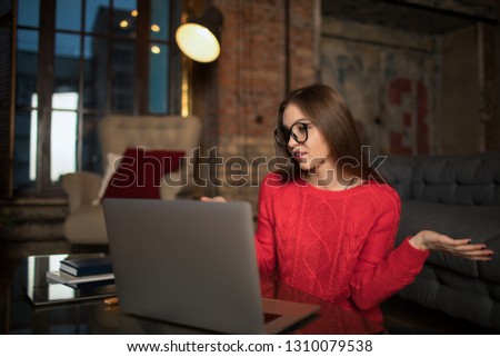 Attractive woman with stylish look having online conference via laptop computer during freelance work, sitting indoors modern co-working space. Female shooting hands don't know gesture 