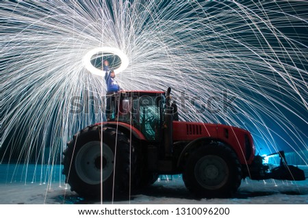Man sparks on the background of a red tractor, steel wool photo, sparks on a long exposure