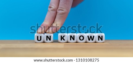 Dice form the word "UNKNOWN" while two fingers push the letters "UN" away in order to change the word to "KNOWN". Royalty-Free Stock Photo #1310108275