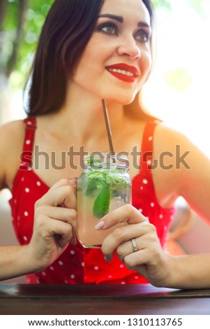 Young brunette woman holding a mason jar in her hand with a mojito. Summer drink concept