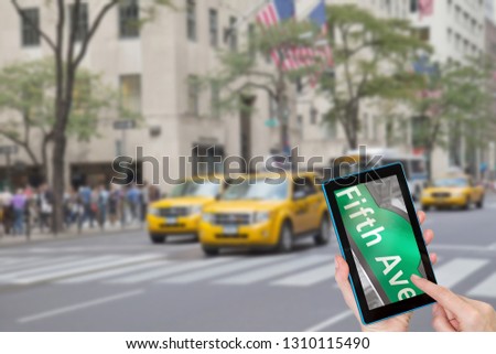Female finger touching tablet with sign Fifth Avenue in the touchscreen. Intentionally blurred image of a Fifth Avenue (NYC) is in the background. All potential trademarks are removed.