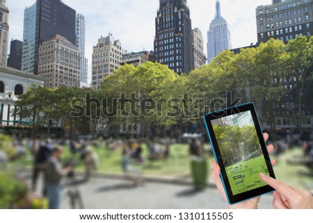 Female finger touching tablet with empty Bryant Park picture in the screen. Intentionally blurred image of a Bryant Park (NYC) is in the background. All potential trademarks are removed.