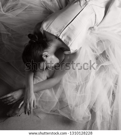 Black and white rear view of beautiful ballet dancer stretching on floor with tutu, conceptual romantic emotional expression, flexibility, stage indoors. Artistic female romantic performance, elegant.