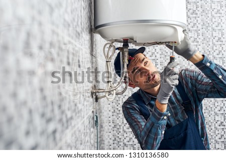 Almost done. Worker set up electric heating boiler at home. Close-up of young handyman Royalty-Free Stock Photo #1310136580