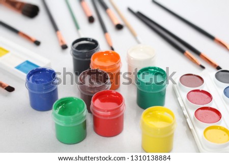 On a white table are brushes, watercolor paints and gouache. The picture is multicolored and very bright. Suitable for artists and students.