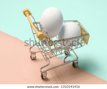 Chicken eggs in mini shopping trolley on colored pastel background
