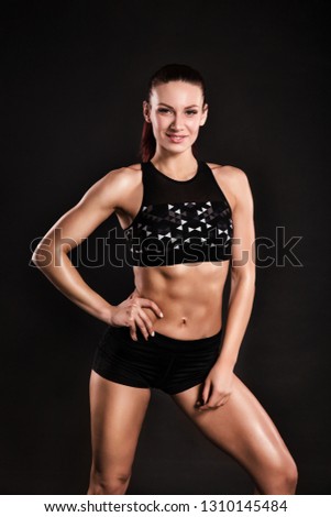Strong girl posing on black background. Photo of fitness model with feminine physique in silhouette
