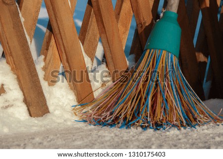 A plastic broom with multicolored bristles of the pile stands in the snow. The concept of cleaning  the area of snow in the winter.Close-up of the object with space to copy outside 