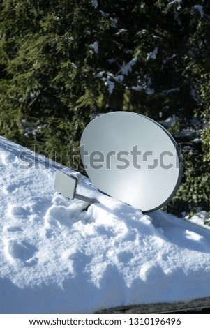 Close up on a satellite antenna dish on a snow covered roof, with space for text on top and bottom