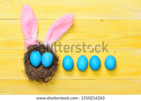 set of traditional eggs painted in blue color in line with nest and pink rabbit ears on yellow vintage wooden background. Happy Easter concept