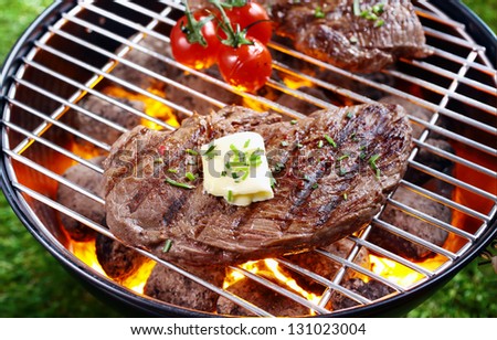 High angle view of a portion of lean steak topped with butter and herbs grilling over a glowing fire in a portable barbecue outdoors on grass