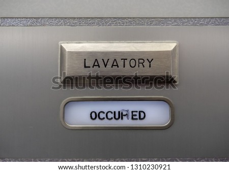 Close up of an occupied sign on an aircraft bathroom door indicating the bathroom is in use. The word "occupied" is slightly obscured by smeared ink in the middle of the word