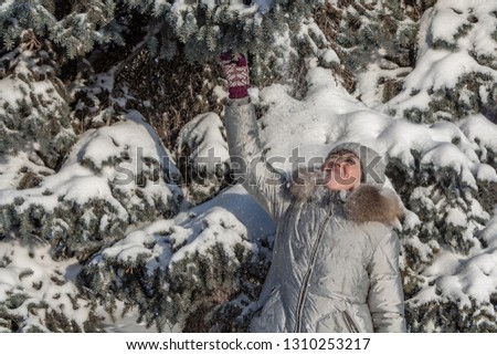 A woman with white frozen eyelashes and red cheeks in a gray hat and gray coat is in a winter park