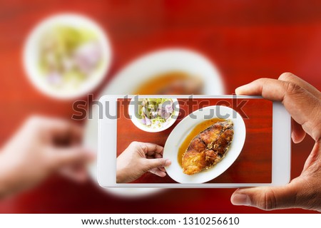 Customer hand take pictures of employees putting fried fish with dipping sauce on wooden table with smartphone.